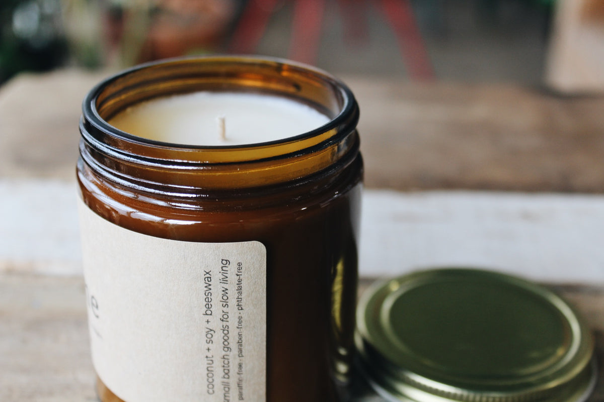Candle in an amber glass jar with a gold lid on a wooden surface