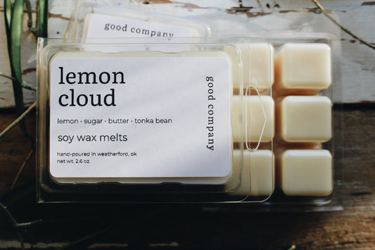 A package of Good Company 'Lemon Cloud' soy wax melts in a clear plastic clamshell container with a white label, showing 6 cream-colored wax cubes inside, set on a rustic wooden surface.
